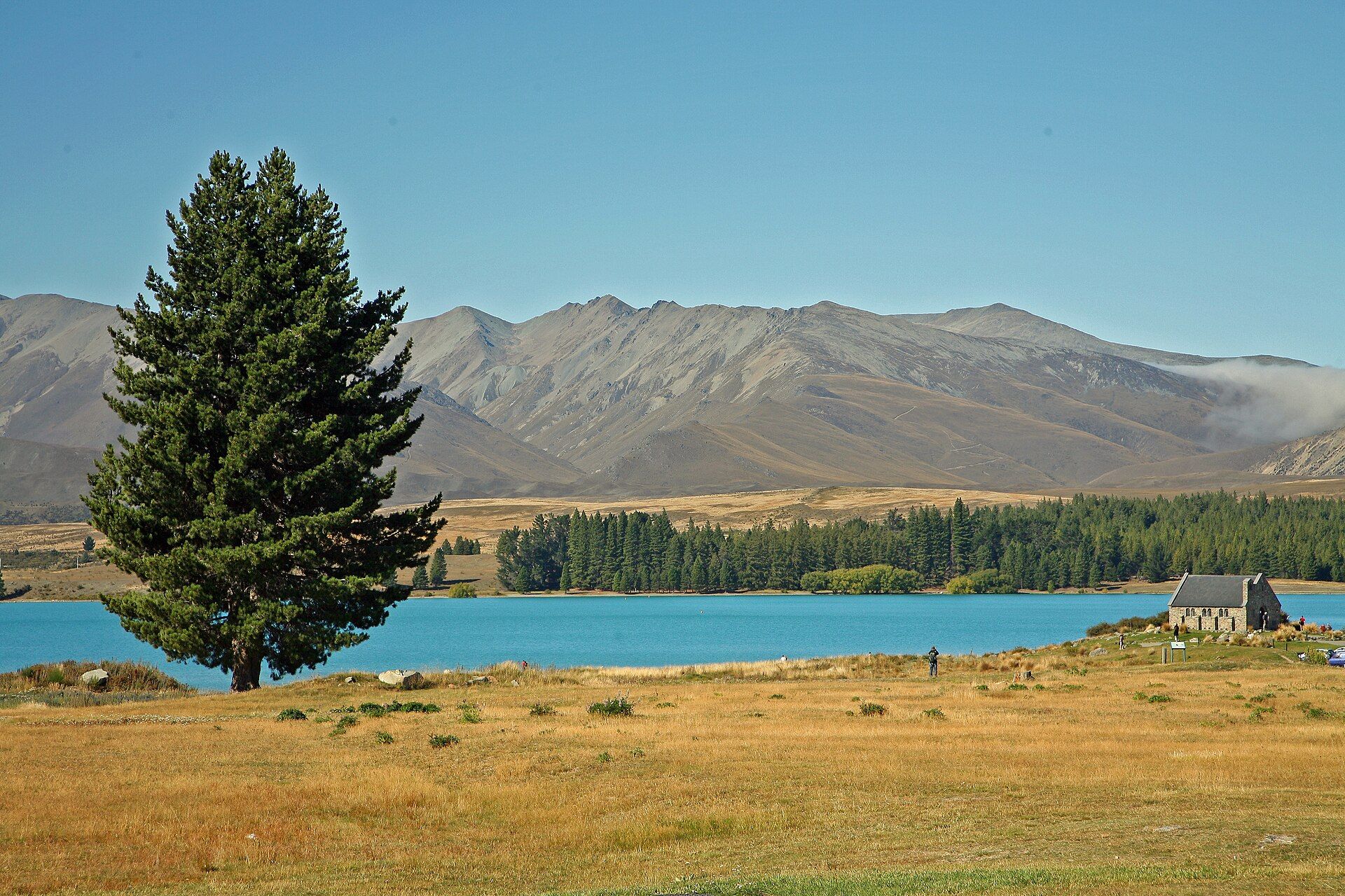 Turquoise Lake Tekapo with the stone Church of the Good Shepherd on the shore and tussock-covered mountains behind, Mackenzie Basin, New Zealand