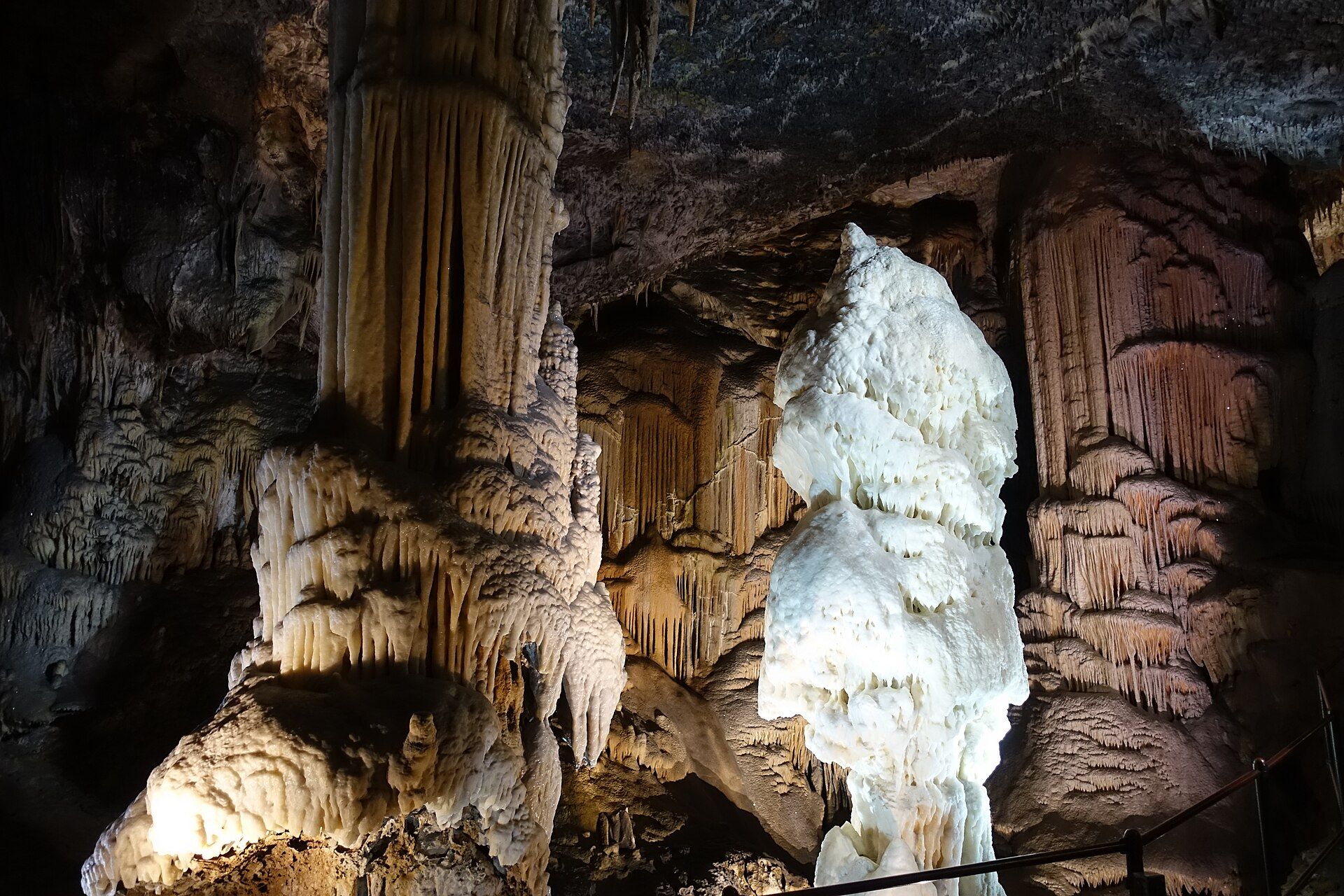 The bright-white Brilliant stalagmite beside a tall, ornate flowstone column, lit inside Postojna Cave, Slovenia