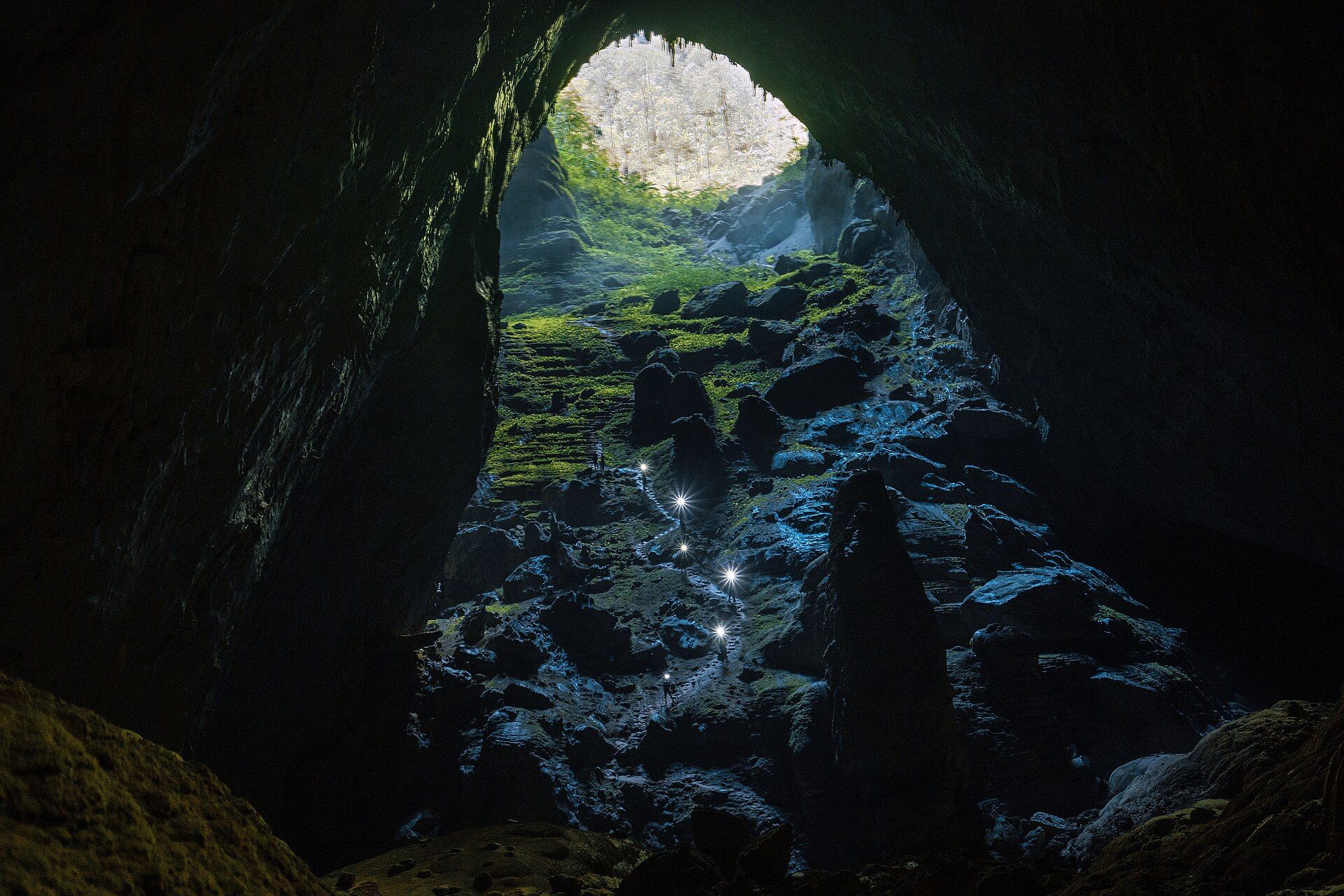 Climbers' headlamps on the boulder slope leading up to a sunlit doline inside Sơn Đoòng Cave, Vietnam
