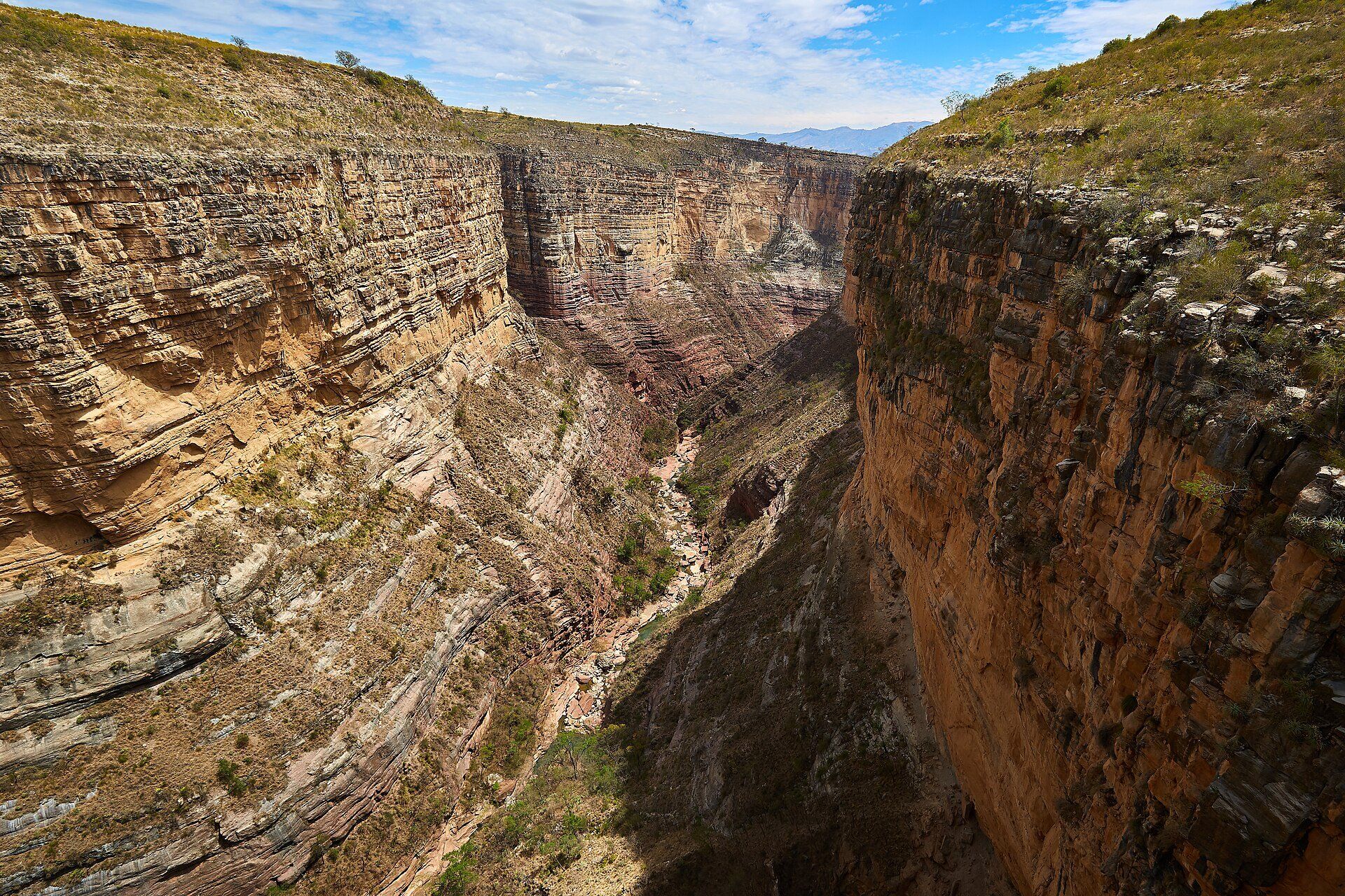 A deep, narrow canyon with layered tan and pink sandstone walls and a dry rocky riverbed at the bottom, under a partly cloudy sky, Torotoro National Park, Bolivia